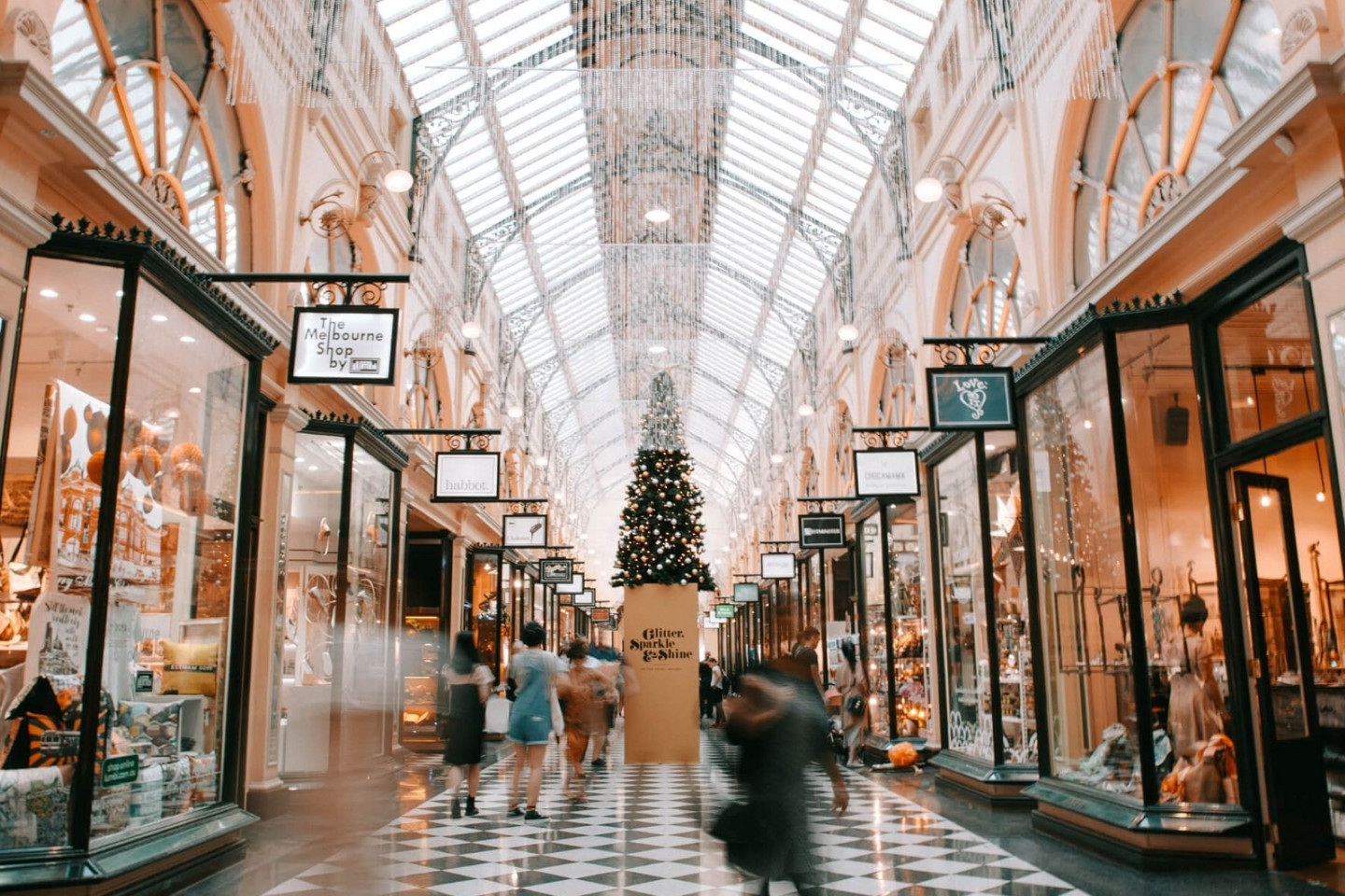 Einkaufspassage mit Glasdach, festlich dekorierten Schaufenstern und großem Weihnachtsbaum, Menschen schlendern hindurch.