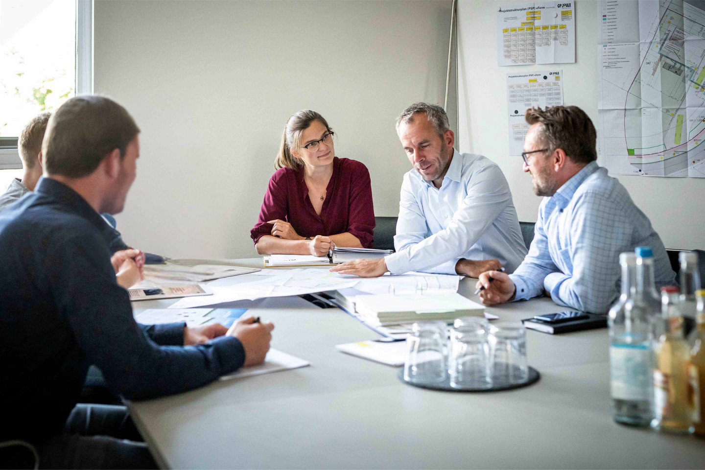 Fünf Personen sitzen im Besprechungsraum und diskutieren Pläne und Unterlagen am Tisch.