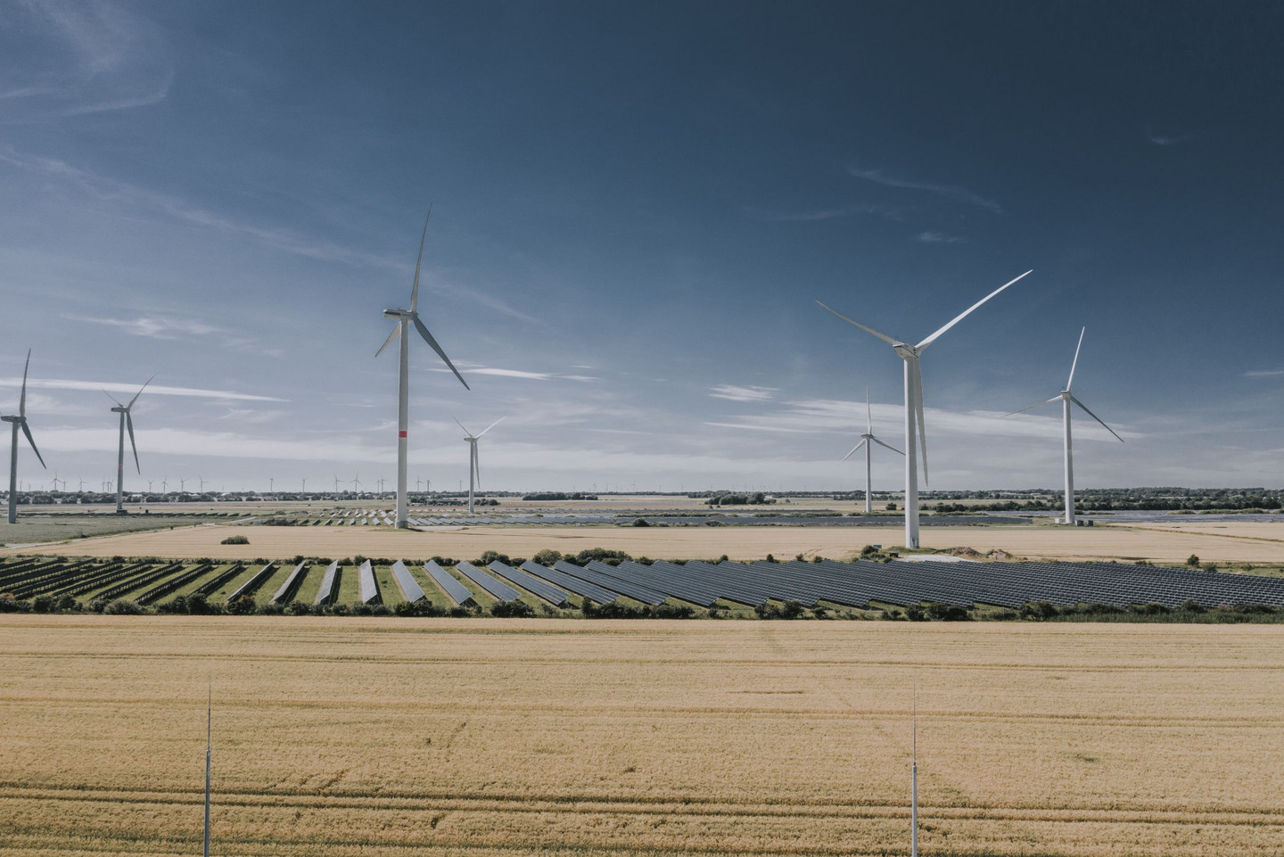 Windräder und große Solarfelder in einer weitläufigen Landwirtschaftslandschaft unter blauem Himmel.